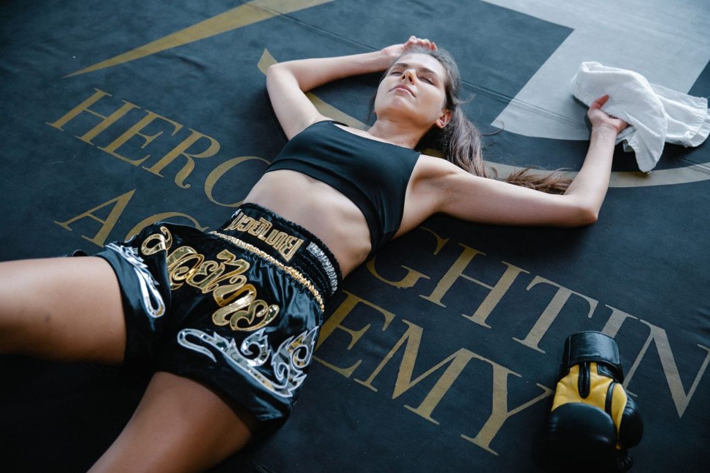 Young woman in boxing attire relaxing on gym mat after training session.