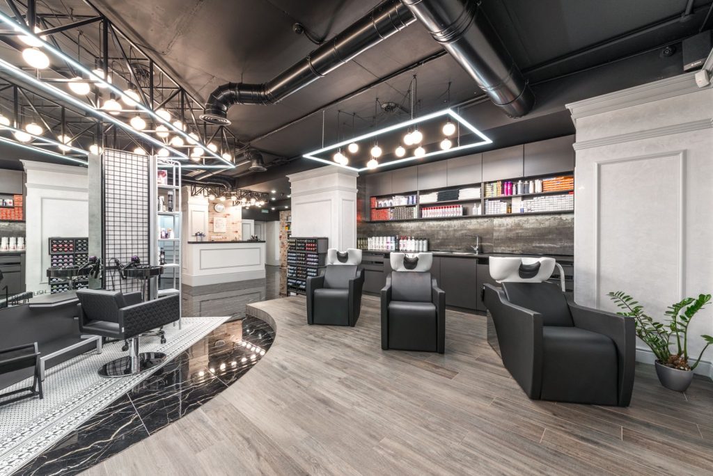 Comfortable backwash chairs with sinks near potted plant placed in contemporary beauty salon with bright illumination and abundance of cosmetology products