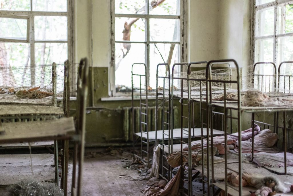 A dusty, abandoned room with dilapidated metal beds and broken windows, showing decay.