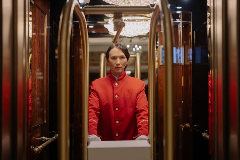 Bellboy in red uniform with luggage cart in luxurious hotel setting.