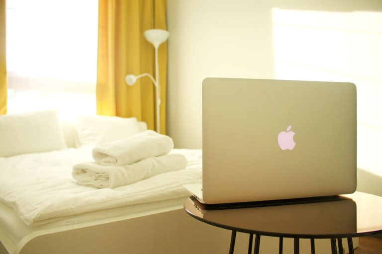 Bright and contemporary bedroom with a laptop, luxurious bed linens, and yellow curtains enhancing the modern design.