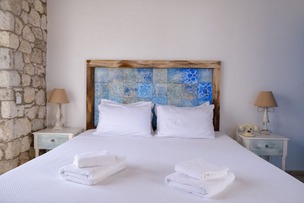 Stylish hotel room with a double bed, white linens, blue headboard, and rustic elements for a relaxing stay.