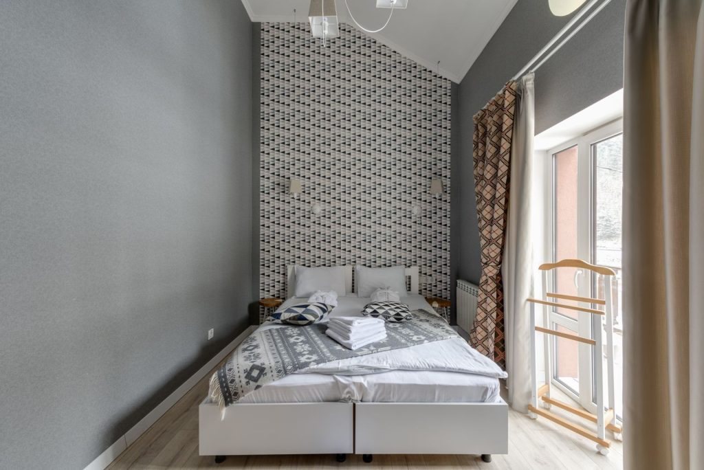 A modern hotel room featuring a double bed, patterned wallpaper, and ample natural light.