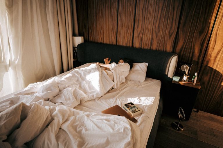 A comfortable hotel room featuring a woman sleeping under soft blankets, basking in morning sunlight.