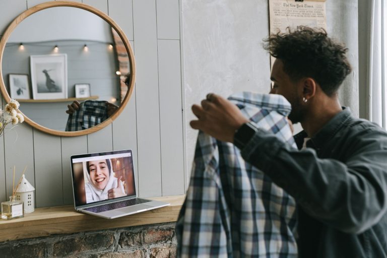 A man holding a plaid shirt engages in a video call on a laptop, capturing modern virtual communication.