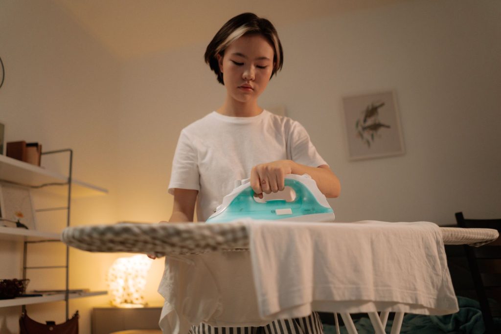 A young woman ironing a white shirt at home, focusing on casual house chores.