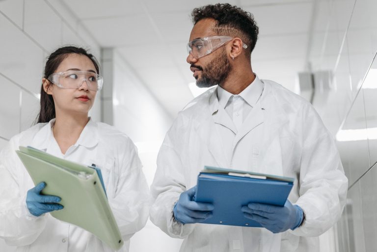 Two scientists in protective gear discuss research in a laboratory setting, focused on collaboration and safety.
