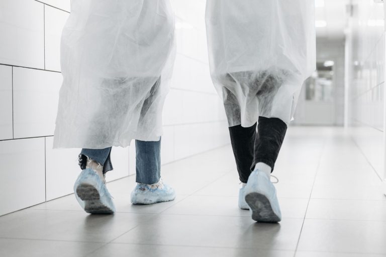Two individuals in lab coats walking in a sterile laboratory corridor.