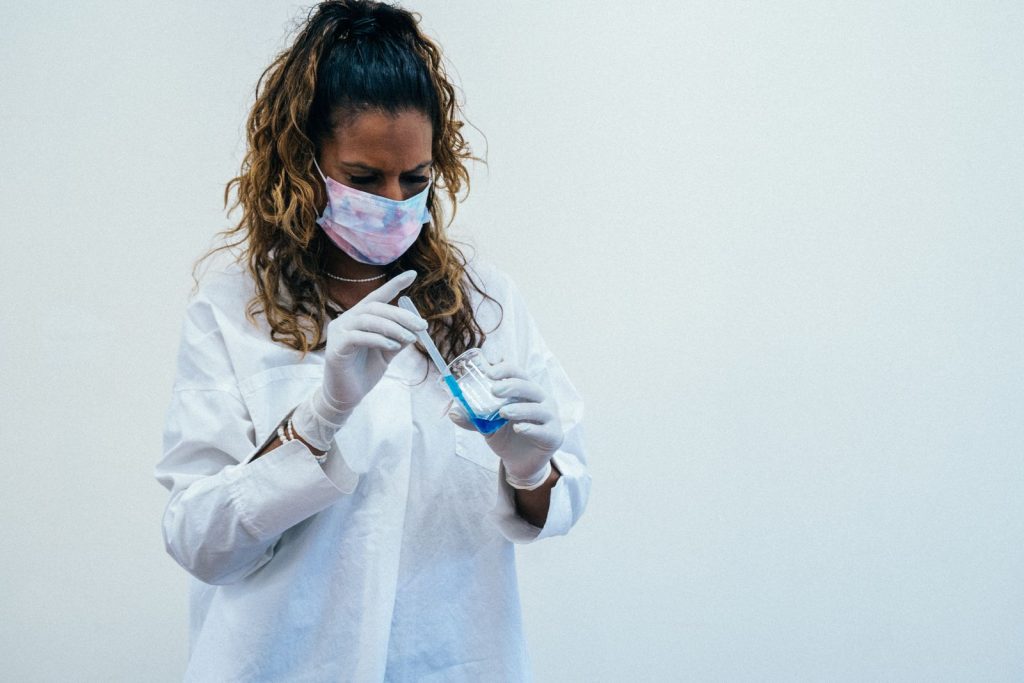 Woman scientist wearing a facemask and gloves conducting an experiment with blue liquid in a lab.