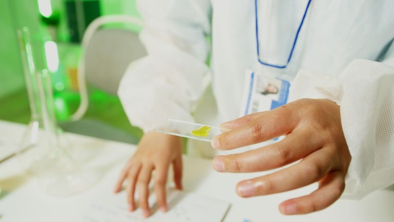 Researcher in a lab coat holding a glass slide, conducting an experiment.