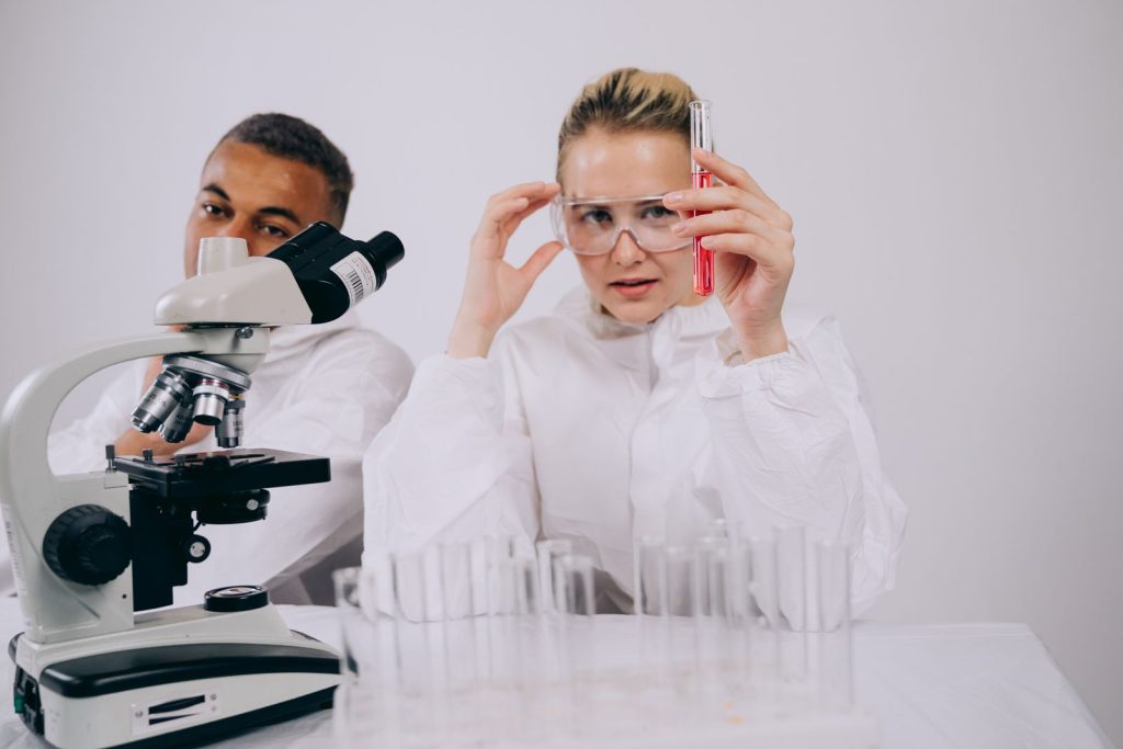 Two scientists working with a microscope and test tubes in a lab.