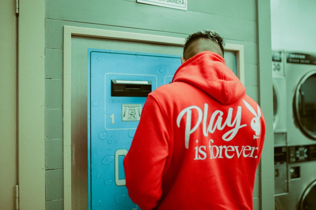 Back view of a person in a red hoodie using a laundry machine indoors.