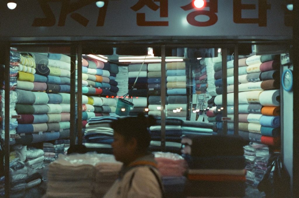 A customer walks by a brightly lit fabric shop filled with vibrant fabric rolls.