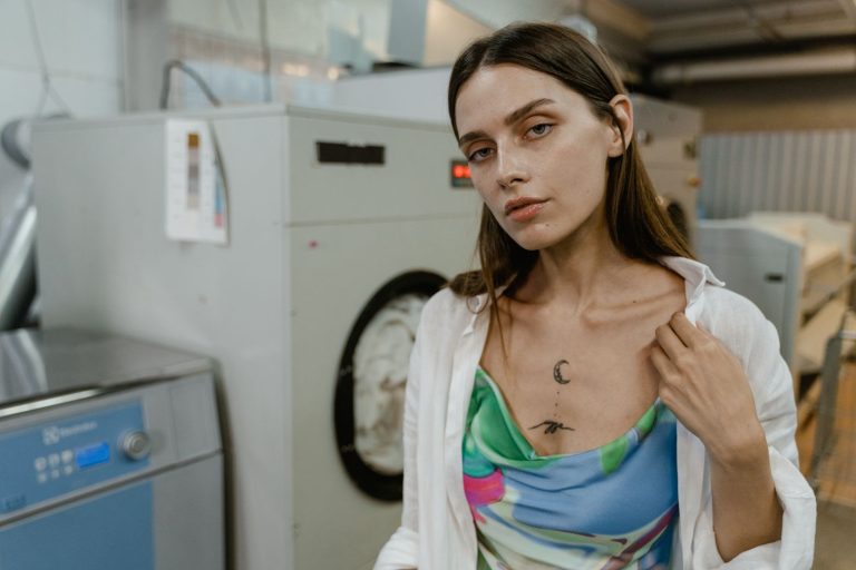 Stylish woman posing in front of industrial washing machines in a laundromat.
