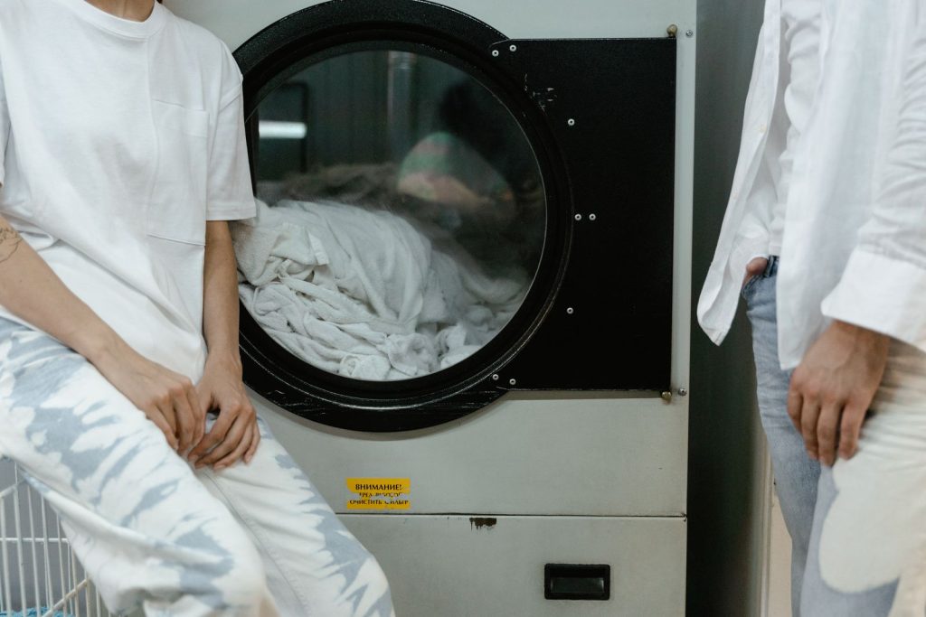Adults in white clothes using a washing machine in a laundry facility.