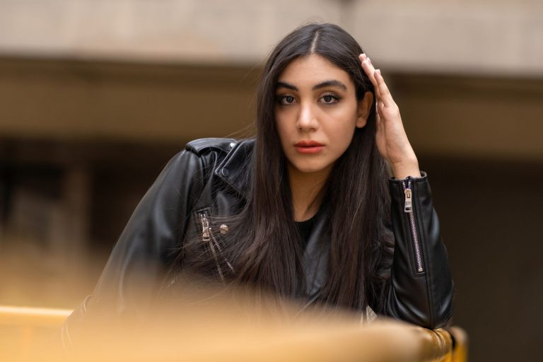 Confident woman in black leather jacket poses outdoors, exuding modern style.