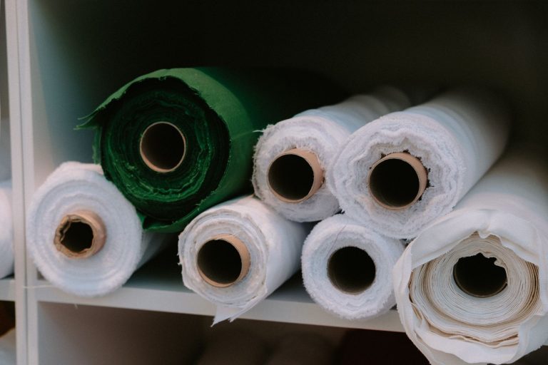Close-up of rolls of fabric in various colors neatly arranged on a shelf in a storage area.