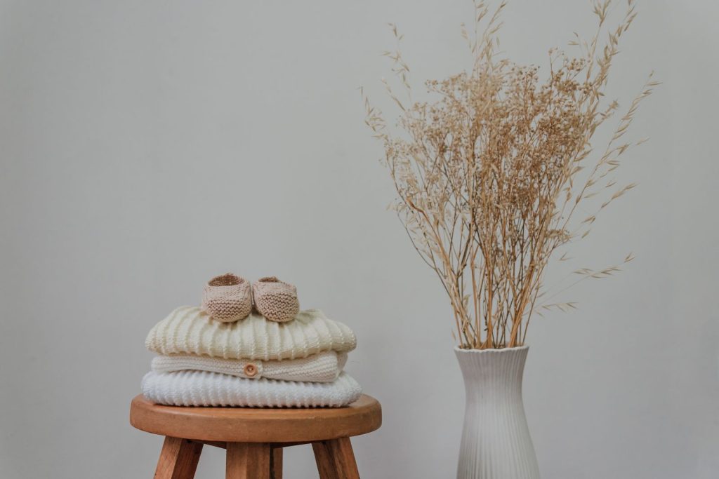 Cozy still life of knitwear, baby booties, and dried flowers on a wooden stool.