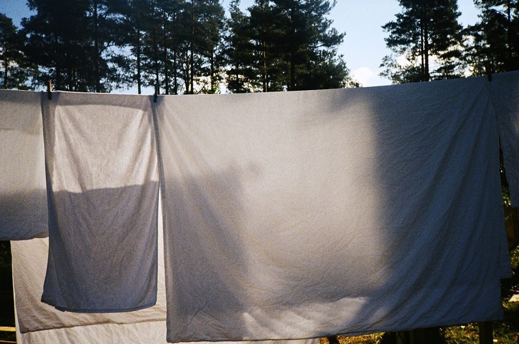Bright sunlight filtering through white linens drying on a clothesline in a forest setting.