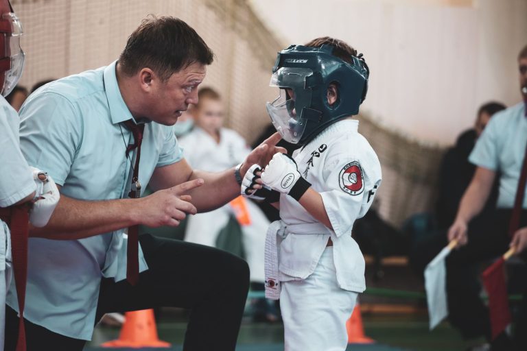 Martial arts coach giving last-minute advice to a young boy in a karate gi before a match.