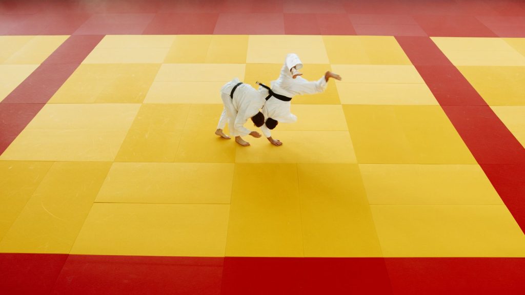 Two martial artists practicing judo techniques on a vibrant yellow and red mat.