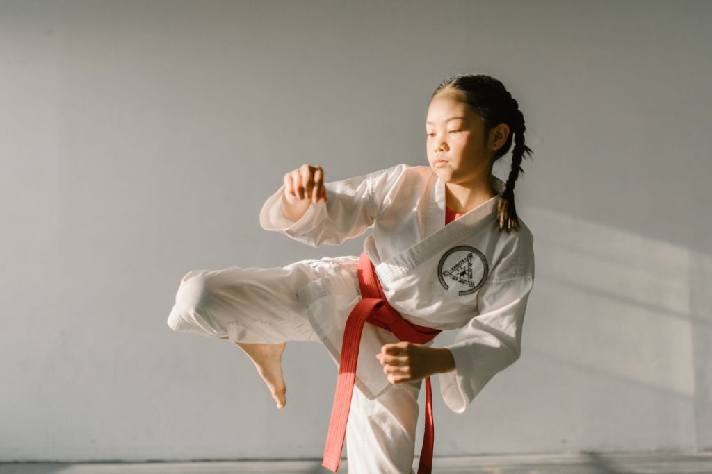 Focused young martial artist practicing a kick in a dobok uniform indoors with natural light.