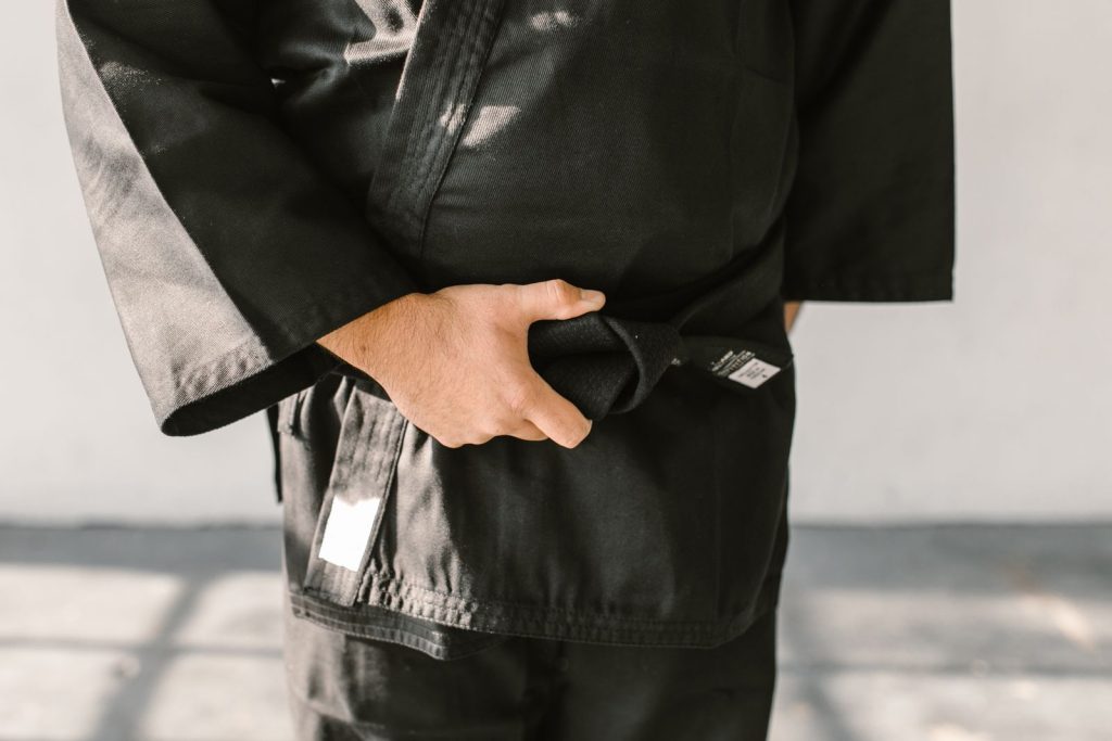 Close-up of a martial artist's hand holding a black belt in a judo uniform indoors.