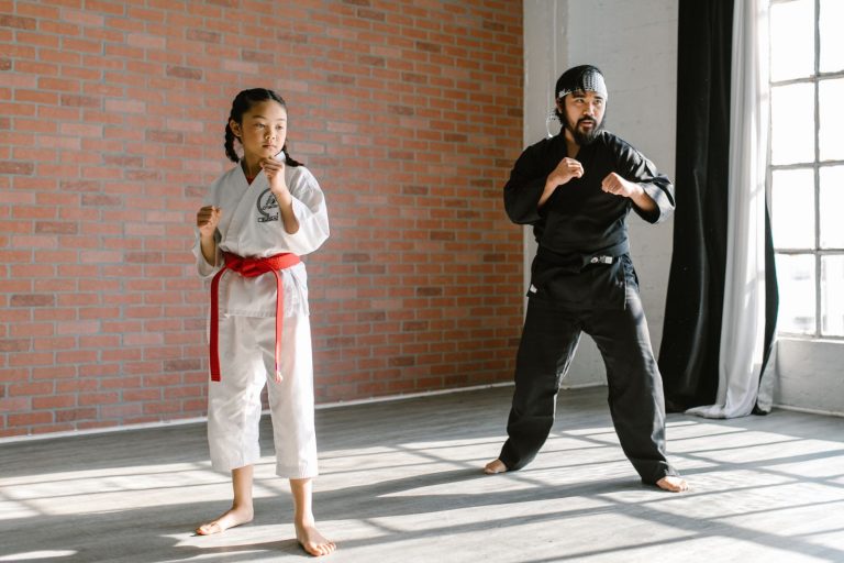 A child and adult practicing martial arts in a bright dojo with a brick wall.