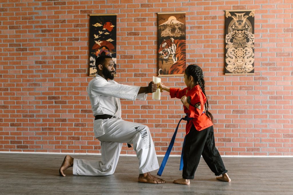 Instructor teaching martial arts to a young student holding a wooden board in dojo.