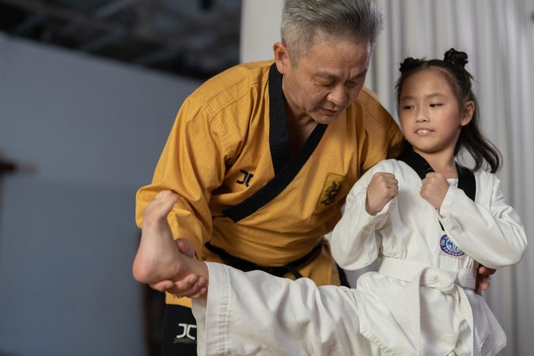 An instructor guiding a young girl in martial arts training indoors.