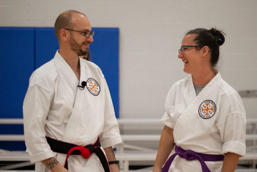 Smiling karate instructors in a dojo sharing a light-hearted moment.