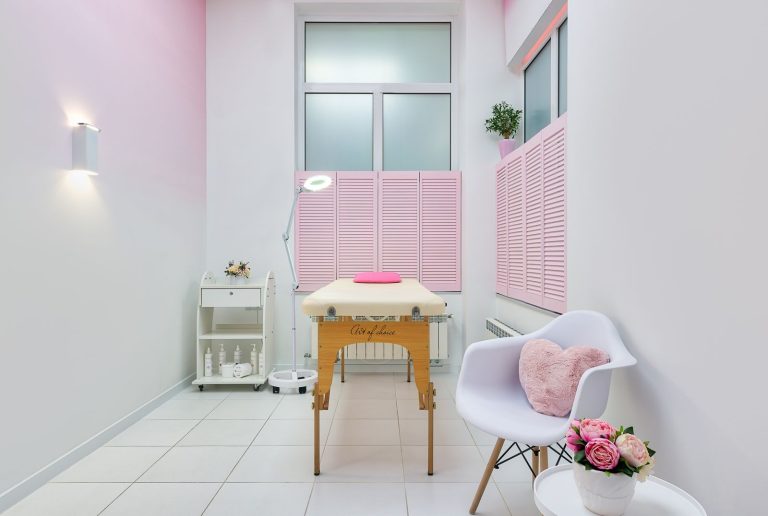 Creative design of massage salon with table between beauty products and armchair against blossoming peonies in pot