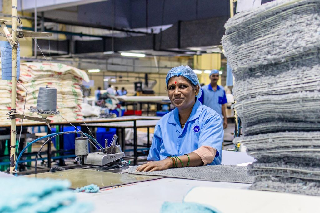 An Indian textile worker in blue uniform smiling at a textile factory.