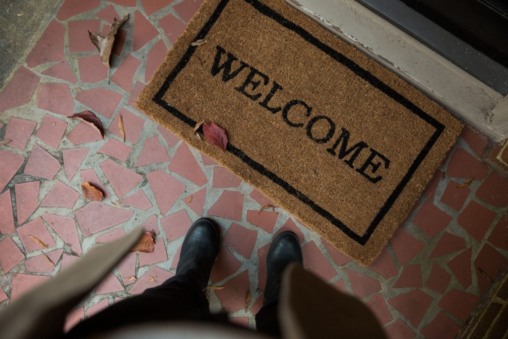 Welcome mat on a tiled porch with boots visible. Perfect for home decor or hospitality themes.