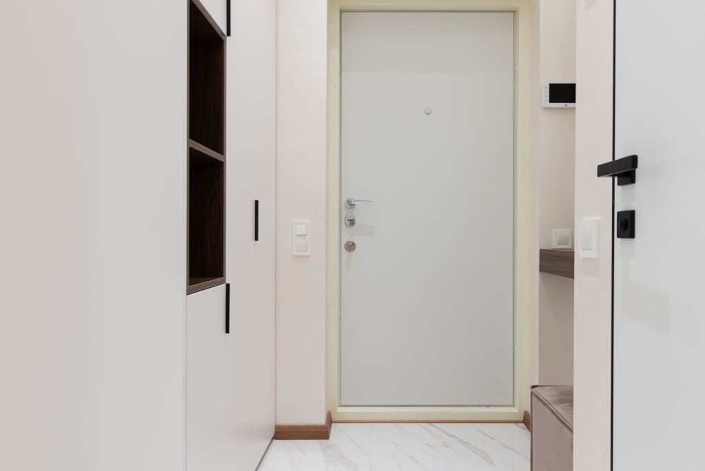 Interior of corridor of modern apartment with white wardrobe and wooden shelves near entrance door
