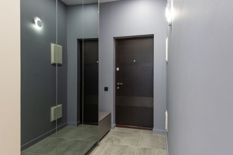 Interior of light hallway with gray walls and closet with mirror doors placed on parquet near door