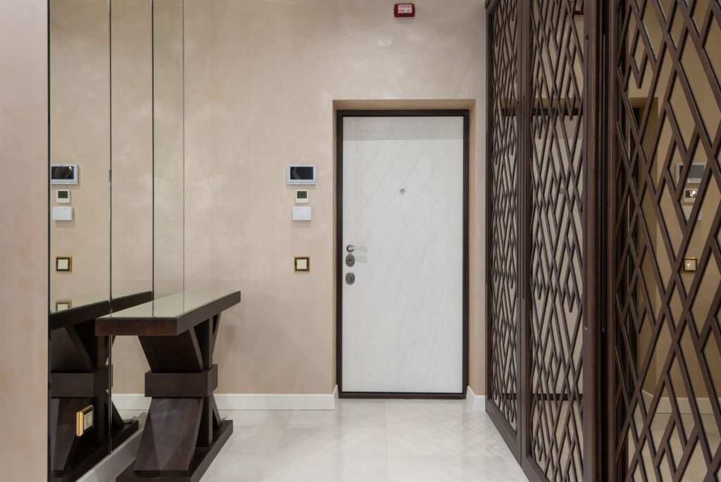 Elegant hallway interior featuring mirrors, modern door, and stylish furniture in neutral tones.