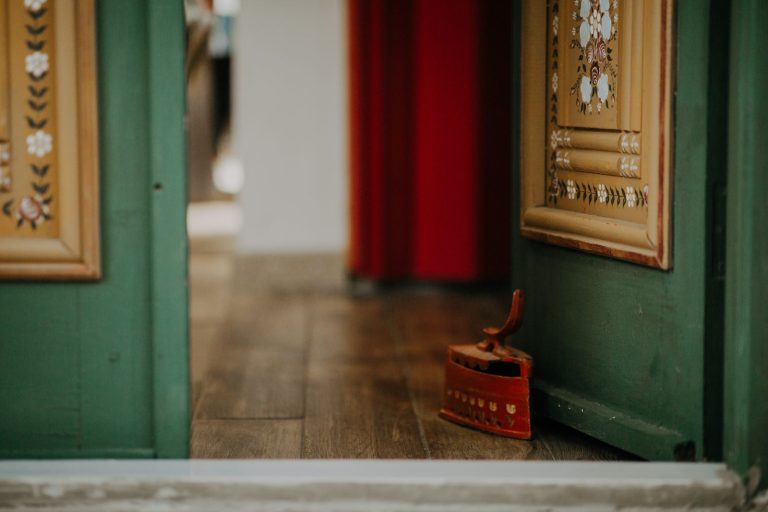 A decorative green door slightly ajar with an antique iron on wooden flooring.
