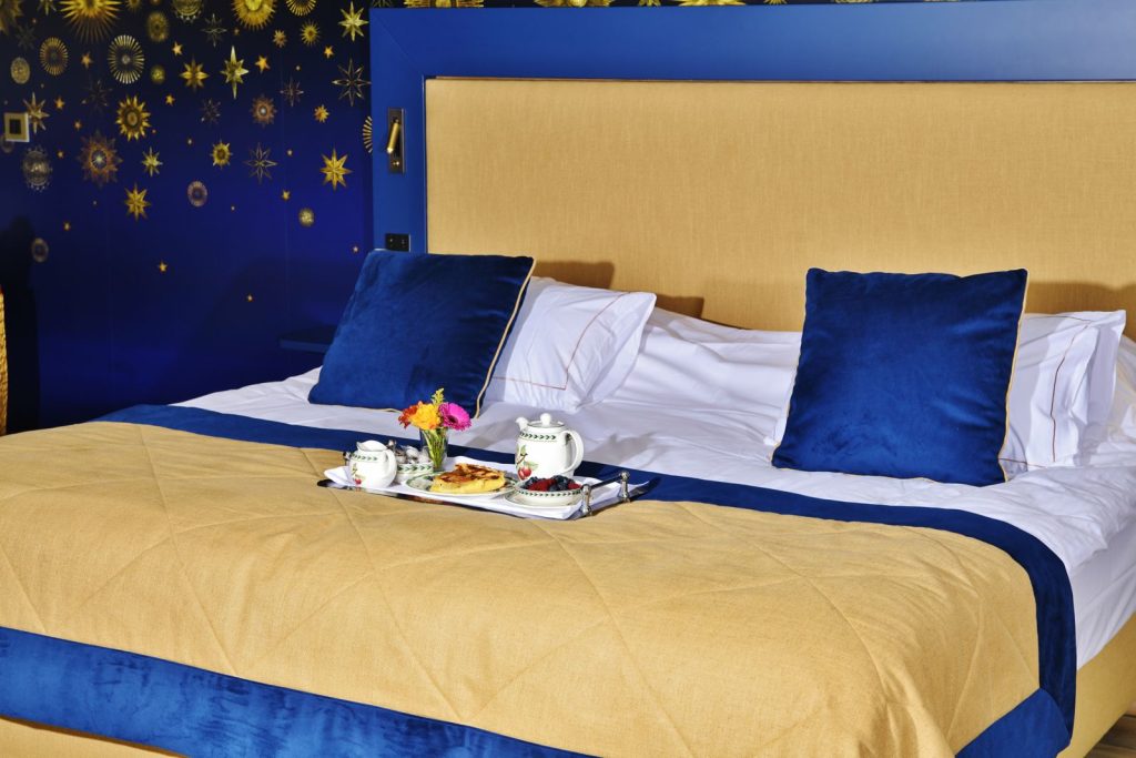 Elegant hotel room with a luxurious breakfast on a blue and gold themed bed.