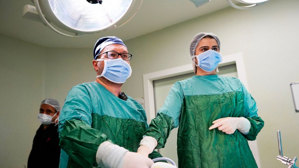 Medical professionals wearing surgical masks and green scrubs in an operating room setting, focused on a procedure.