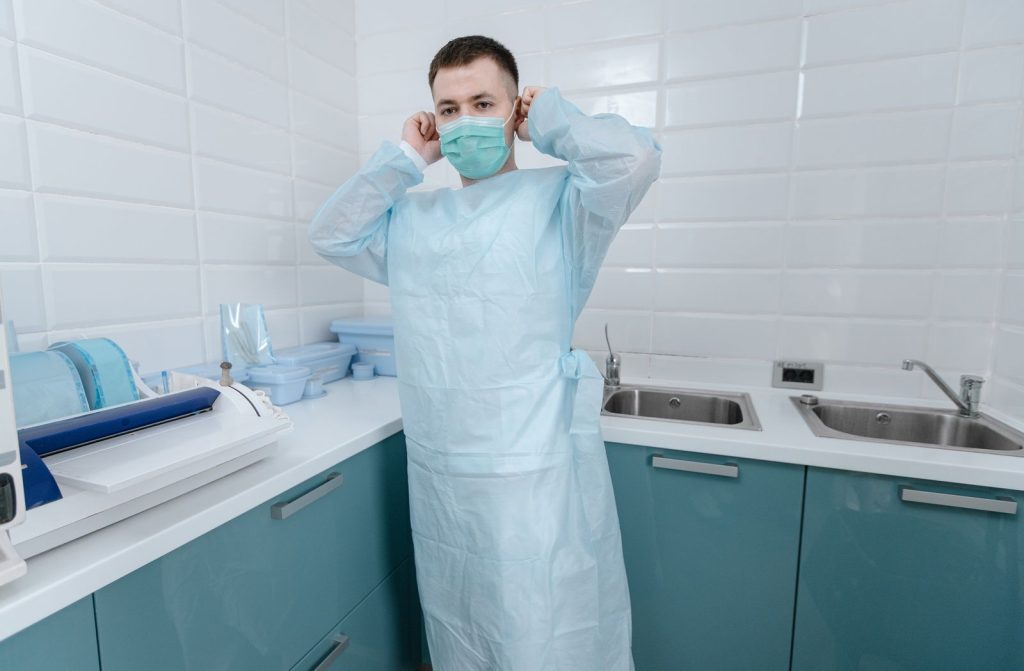 Male healthcare professional wearing protective clothing and mask in a medical facility.
