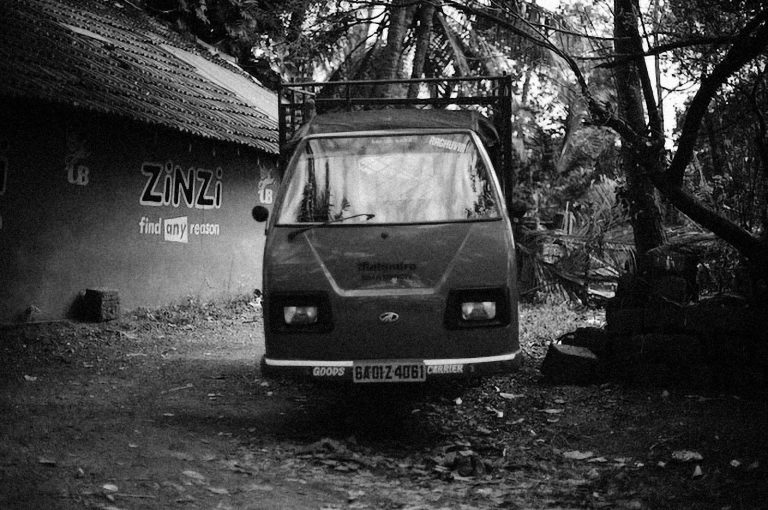 Black and white image of a vintage truck in a rustic outdoor area, surrounded by trees.