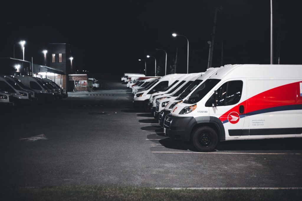 A lineup of white and red delivery vans parked in a lot under streetlights at night.