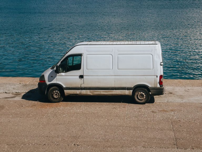A white van parked next to a serene blue sea on a sunny day.