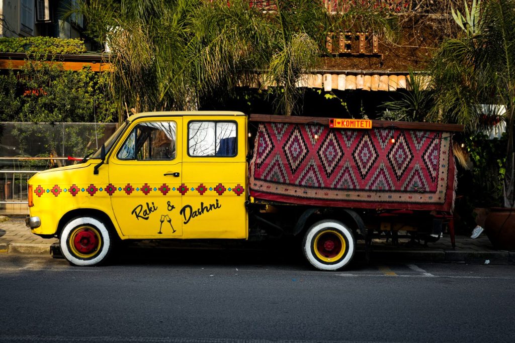 A classic yellow van parked on a cobblestone street in Tirana, Albania, showcasing vibrant Balkan motifs.