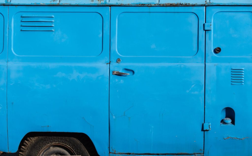Detailed view of a rustic blue van door, highlighting texture and color.