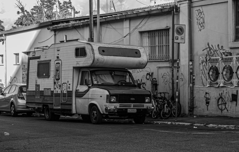 Black and white photo of a vintage camper van parked on an urban street with graffiti walls.