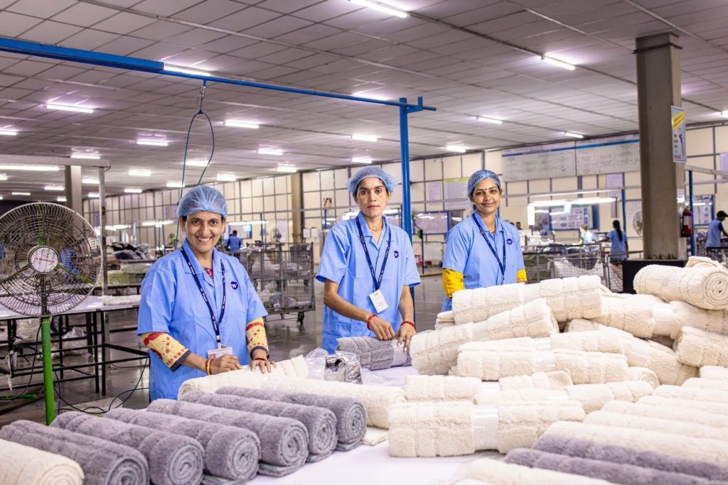 Three female workers in blue uniforms rolling towels in a textile factory.
