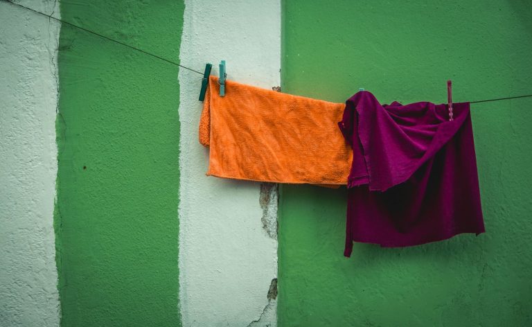 Vibrant orange and red clothes hang on a line against a green wall, creating a striking contrast.