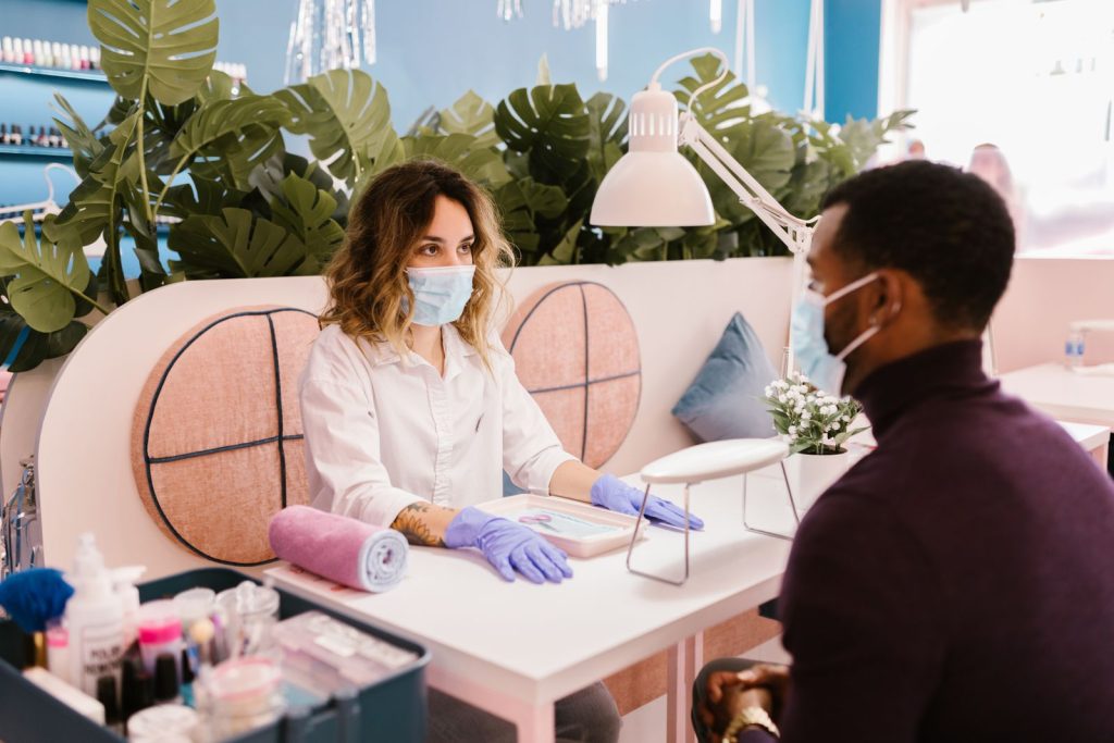 A man receiving a manicure in a stylish nail salon with safety measures.